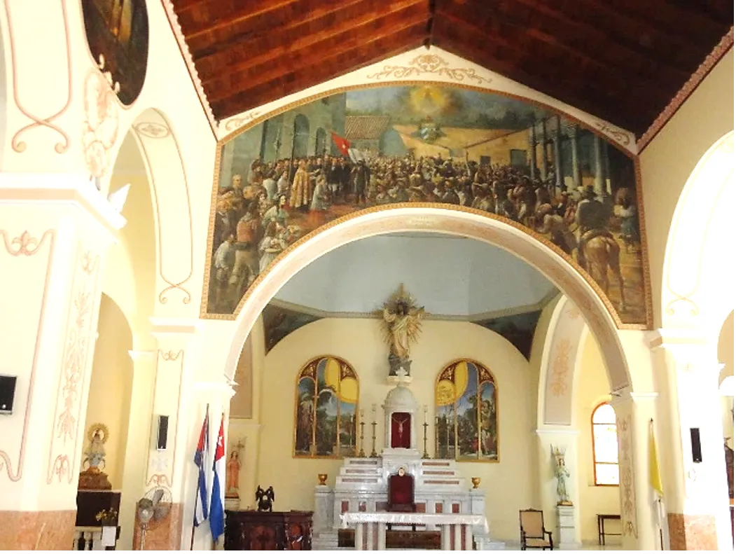 Altar de la iglesia de san Salvador de Bayamo en el que vemos un fresco en la pared, en el  área superior, que representa la procesión con la bandera de Céspedes a la salida del templo